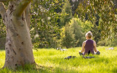 Woman sat on grass in sunshine in yoga pose