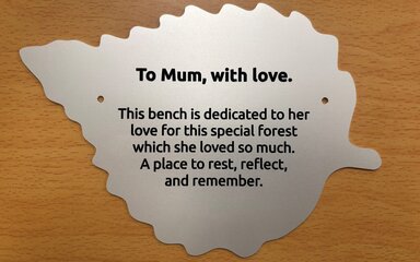 A silver plaque in the shape of a leaf, engraved with a memorial message.