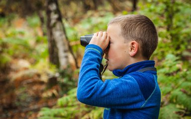 A young boys looks through binoculars in the forest