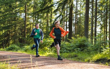 Two boys running along a forest path in the sun.