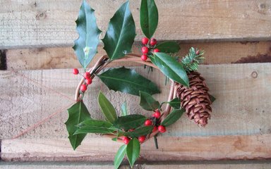 A Christmas wreath made out of green leaves and red berries and a large cone.
