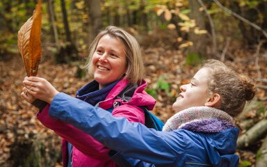 A girl and woman looking at a large autumn leaf they've found