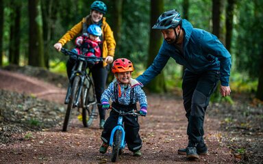 A family of two adults and two young children with bikes in the forest.