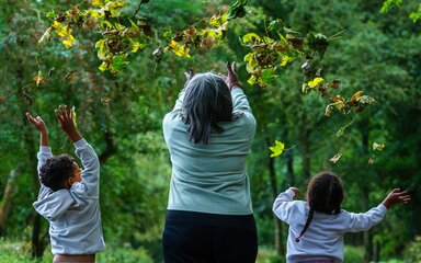 Seen from behind, an adult and two children throwing leaves into the air.