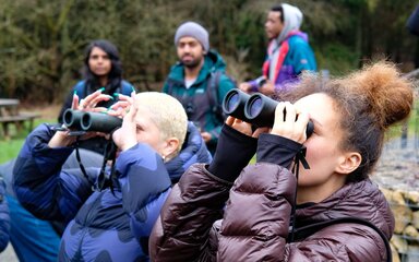 Two women outdoors looking through binoculars.