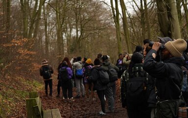 A group of people in autumn woodland, some looking through binoculars.