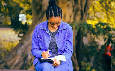 Woman in denim sitting on bench in the forest, writing in a book