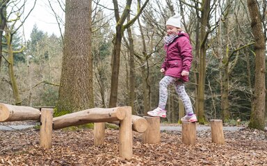 A young girl in winter coat and hat on a woodland obstacle course.