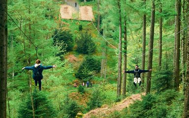 A man and a woman on zip wires through the trees