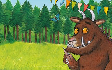 A digital illustration of the Gruffalo standing in the forest with bunting strung above him.