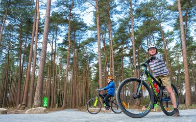 Two boys on bikes on a sufaced cycle trail in the forest.