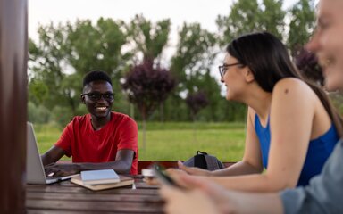 A group of young people gather around a table to have a conversation in a woodland setting.