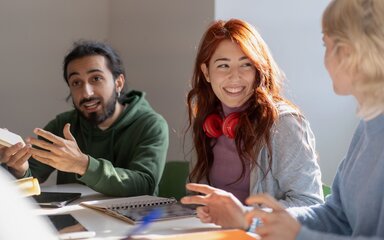 Three young people sit round a desk with notepads discussing an interesting topic.