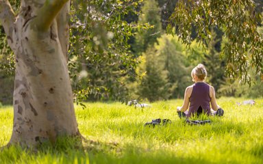 Woman sat on grass in sunshine in yoga pose