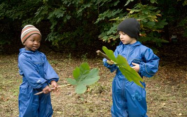 Two children playing with large leaves in the forest 