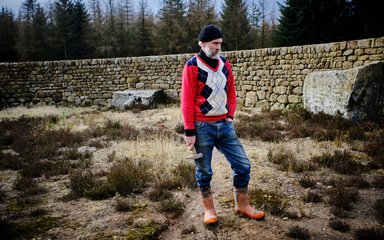 Man stood staring at the ground holding a wooden tool within stone wall maze