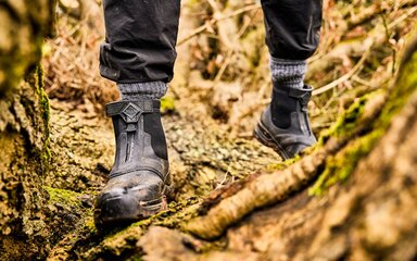 Close-up of a pair of legs from the shins downwards, wearing sturdy boots on rough terrain.