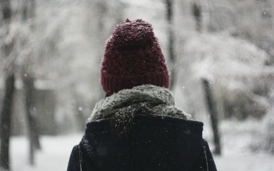 Woman in a red hat and blue coat looking at snow in the forest