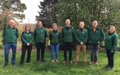 Group of 5 men and 3 women stand in a line wearing Forestry England jumpers. 