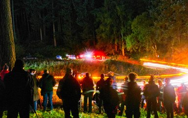 A blur of lights beyond a group of spectators at night rally