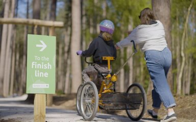 Girl on adapted trike being helped by her mother, riding away to the finish line