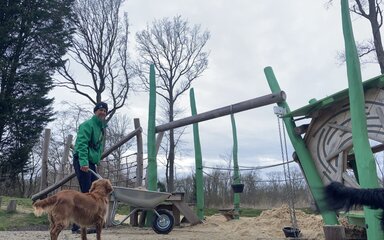 A man and a dog by a play area in the forest.