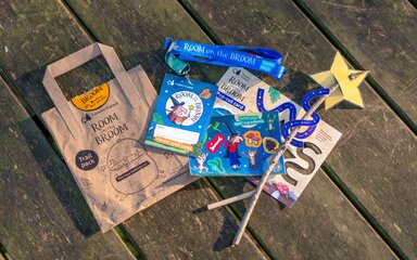 Room on the Broom branded paper bag, lanyard, activity sheet and a magic wand laid out.