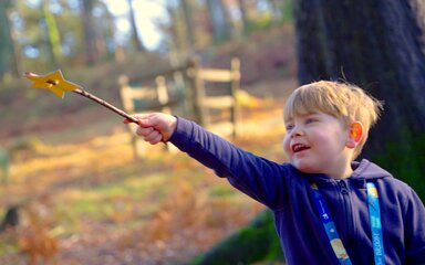 A young boy waving a DIY magic wand in the forest.