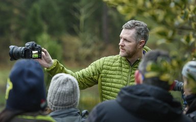 Man standing in a forest showing a group of people a camera