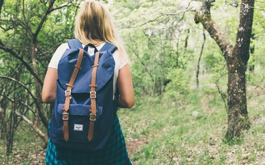 Women with blue backpack walking through spring woodland