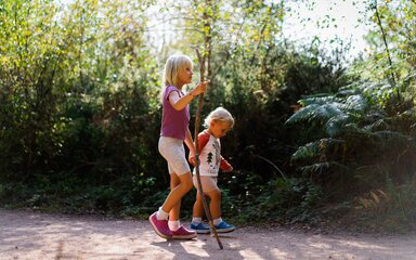 A young girl and boy in shorts and t-shirt, on a forest path in the sun.