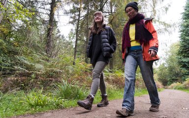 Two women walking along a woodland path in autumn.