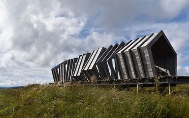 The Nick wooden viewpoint in Kielder Forest, surrounded by moorland grass under a cloudy sky.
