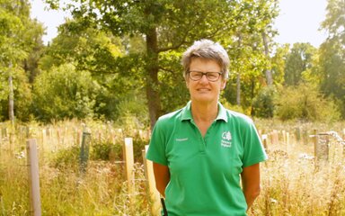 A female volunteer in a green polo shirt stands smiling in the sun