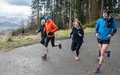 A group of five people running in the forest.