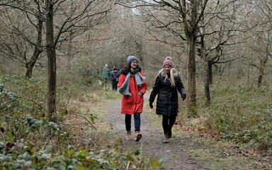 Two women in winter coats, hats and scarves, walking on a forest path.