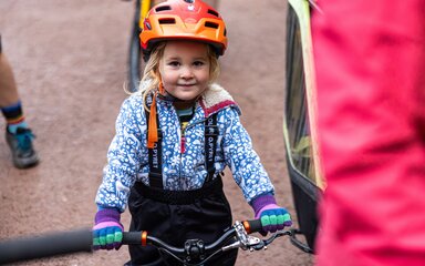 Close-up of a young girl wearing an orange cycling helmet sitting on a bike.