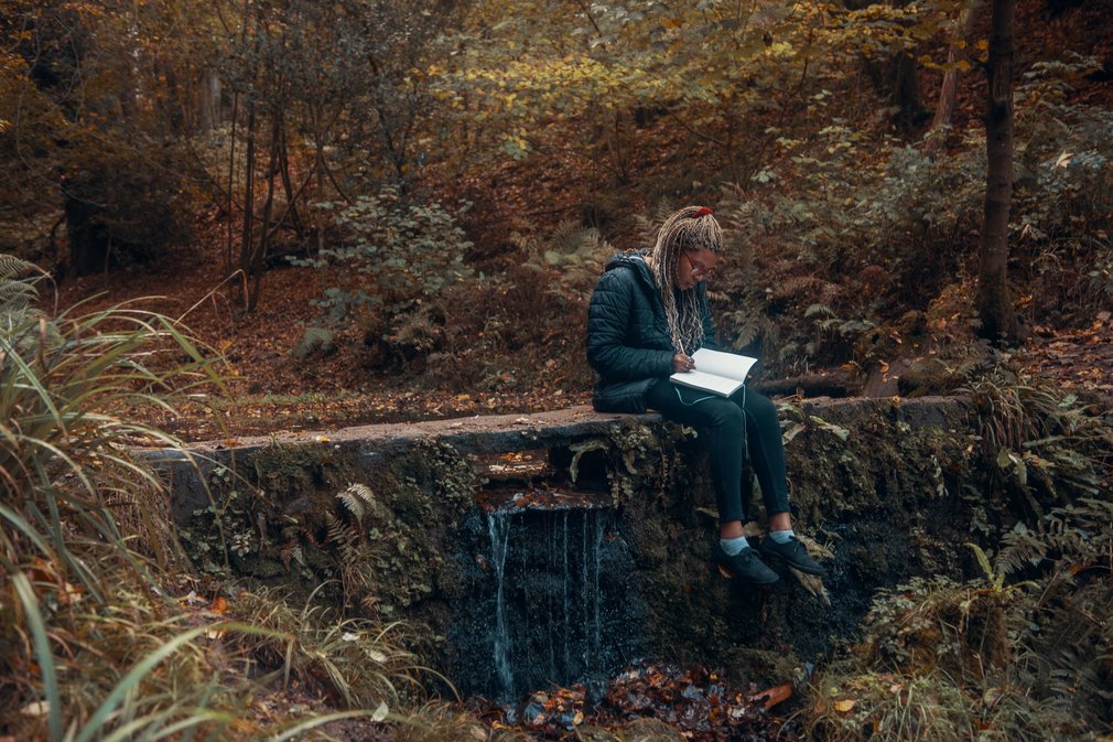 Woman writing in a notepad by a pond