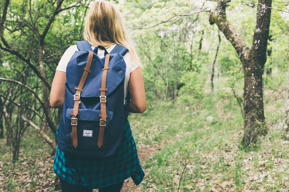 Women with blue backpack walking through spring woodland