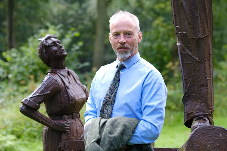 Man in shirt and tie standing in front of metal statue 