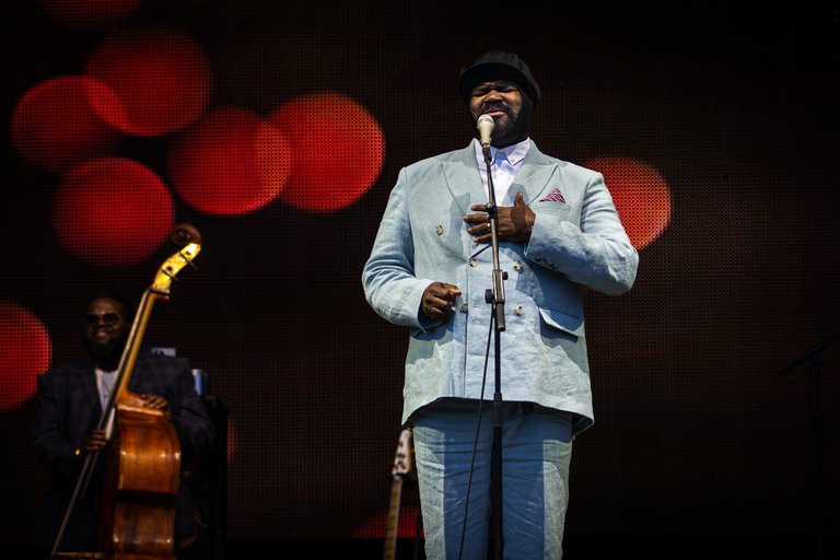 Close-up of male singer Gregory Porter singing into a microphone on stage, wearing a grey suit.