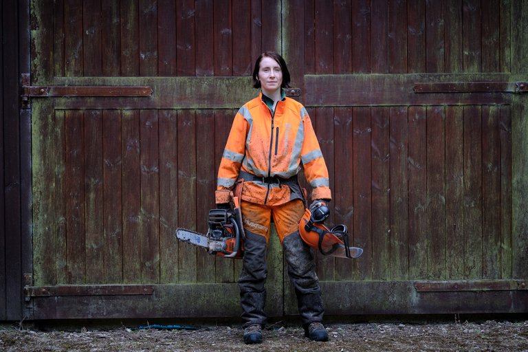 Female forester with chainsaw stood in front of wooden doors 