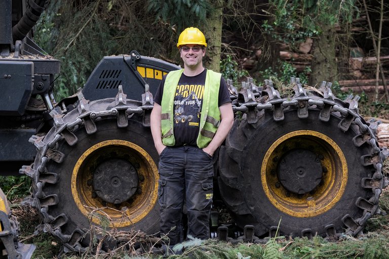 Forester stood in front of forestry machine in high vis and hard hat