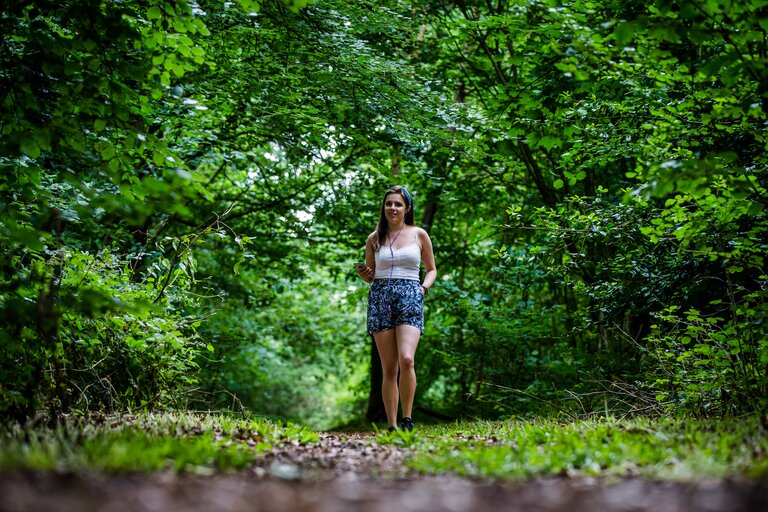 A woman walks along a path surrounded by green trees
