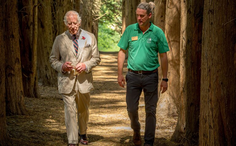 HRH King Charles lll and a Forestry England staff member walking along a narrow enclosed tree lined path