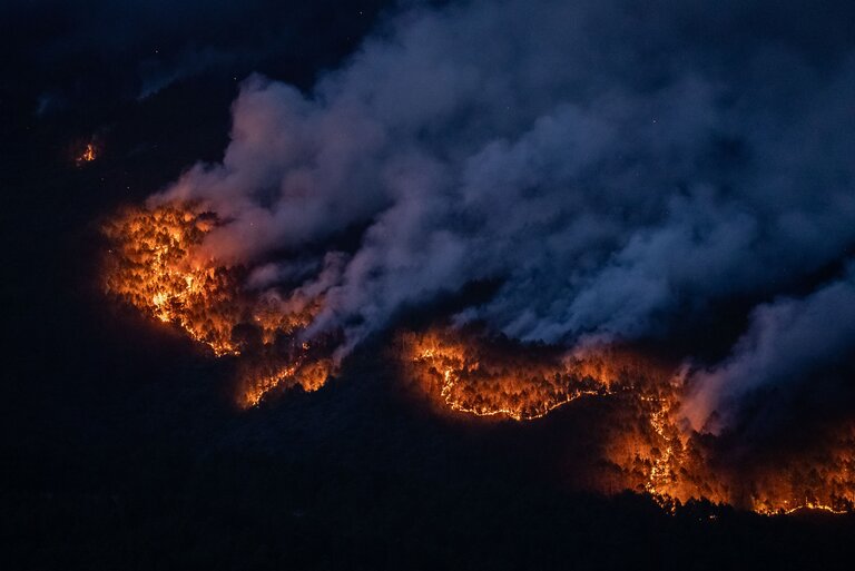 The orange glow of wildfires in the dark, with billowing smoke.