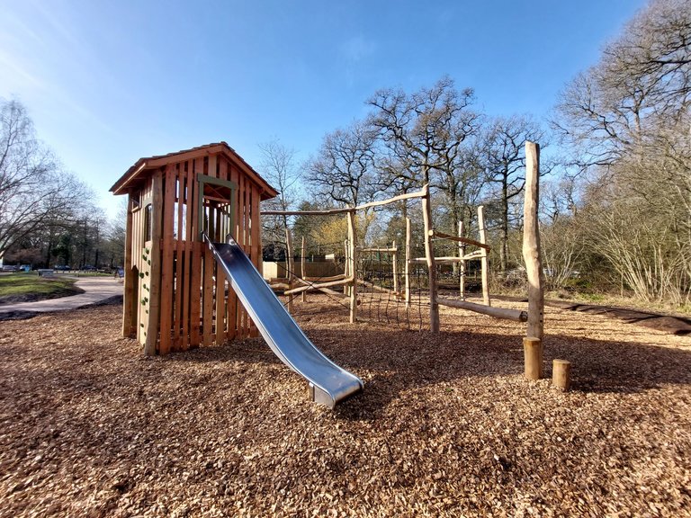 Metal slide coming from wooden play tower with climbing nets and balance beams