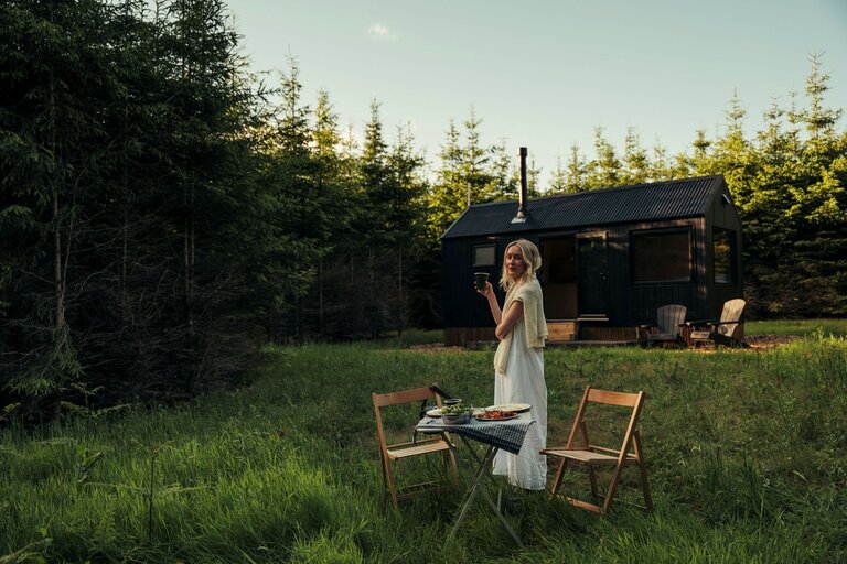 A woman stood outside of a cabin with a dinner set up