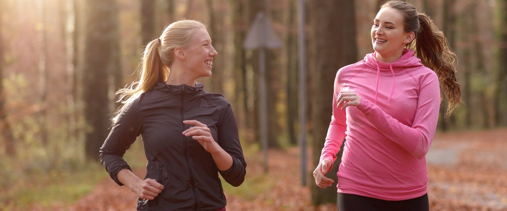 Adults on a run on a woodland trail with autumn leaves