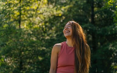 Woman laughing in a sunny forest.